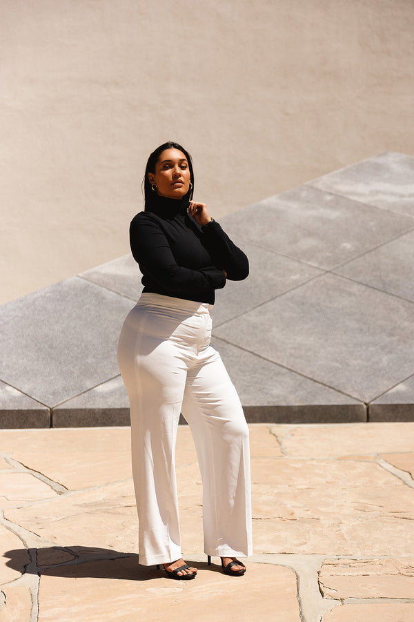 Ambitionist Power Player Turtleneck Bodysuit — model wearing the black turtleneck bodysuit with cream wide-leg trousers